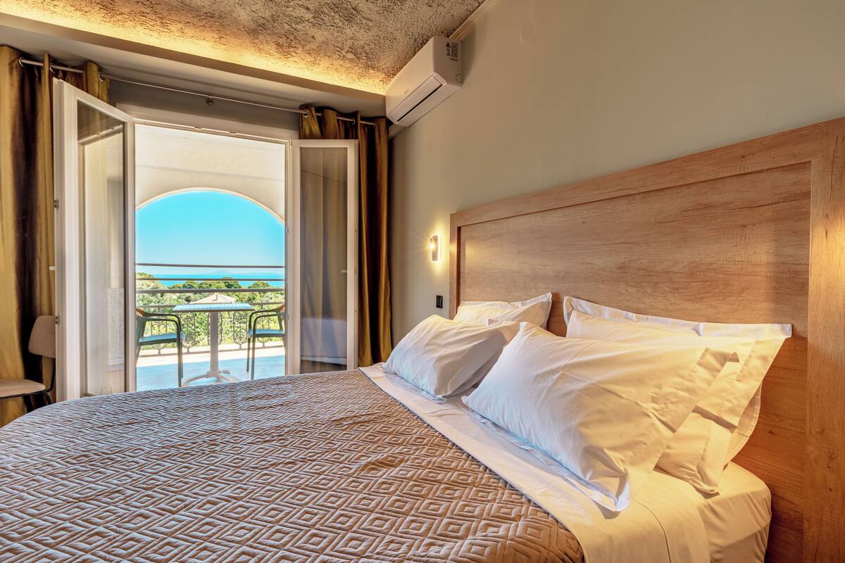A hotel room with a large bed, a wooden headboard, and a balcony with a view of the sea.
