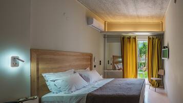 A hotel room with a bed, bedside table, lamp, and a view of the outdoors.