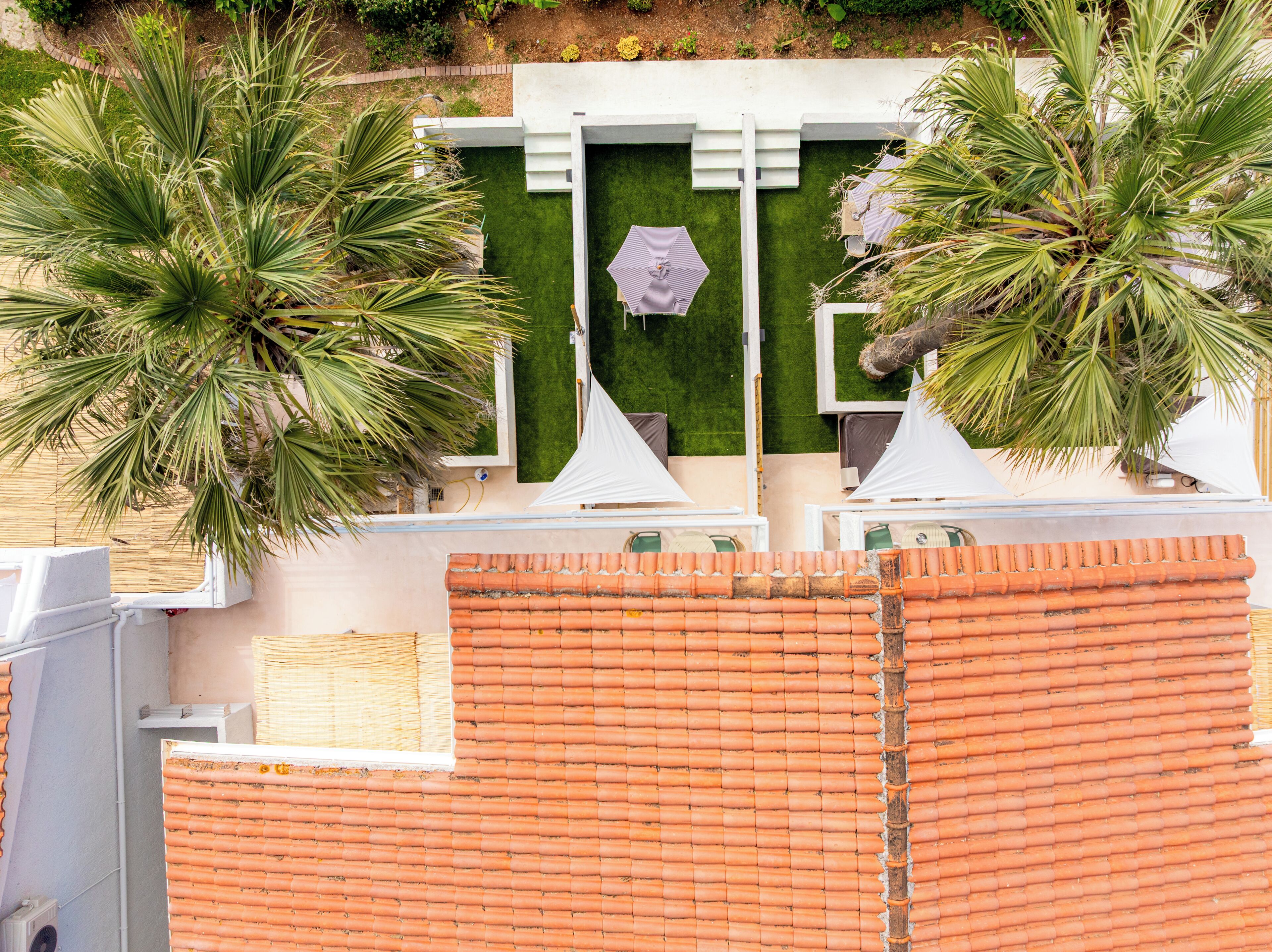 Terraço no topo do prédio com palmeiras, um guarda-sol central e cadeiras de lounge brancas.