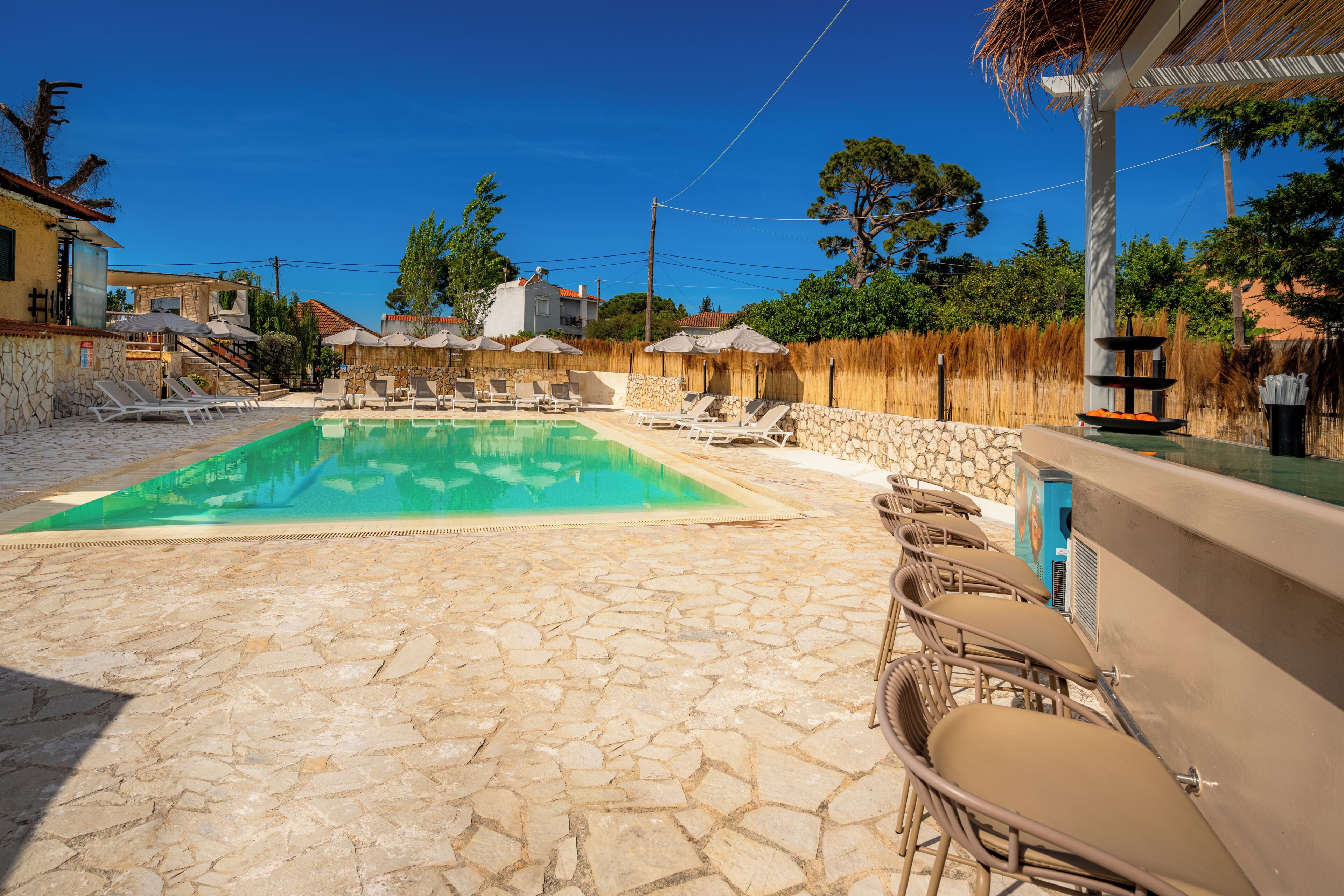 A swimming pool with lounge chairs and umbrellas, stone flooring, and a bar area.