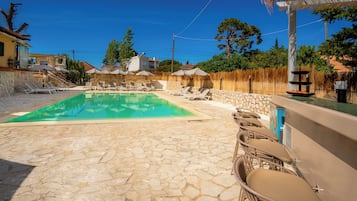 A swimming pool with lounge chairs and umbrellas, stone flooring, and a bar area.