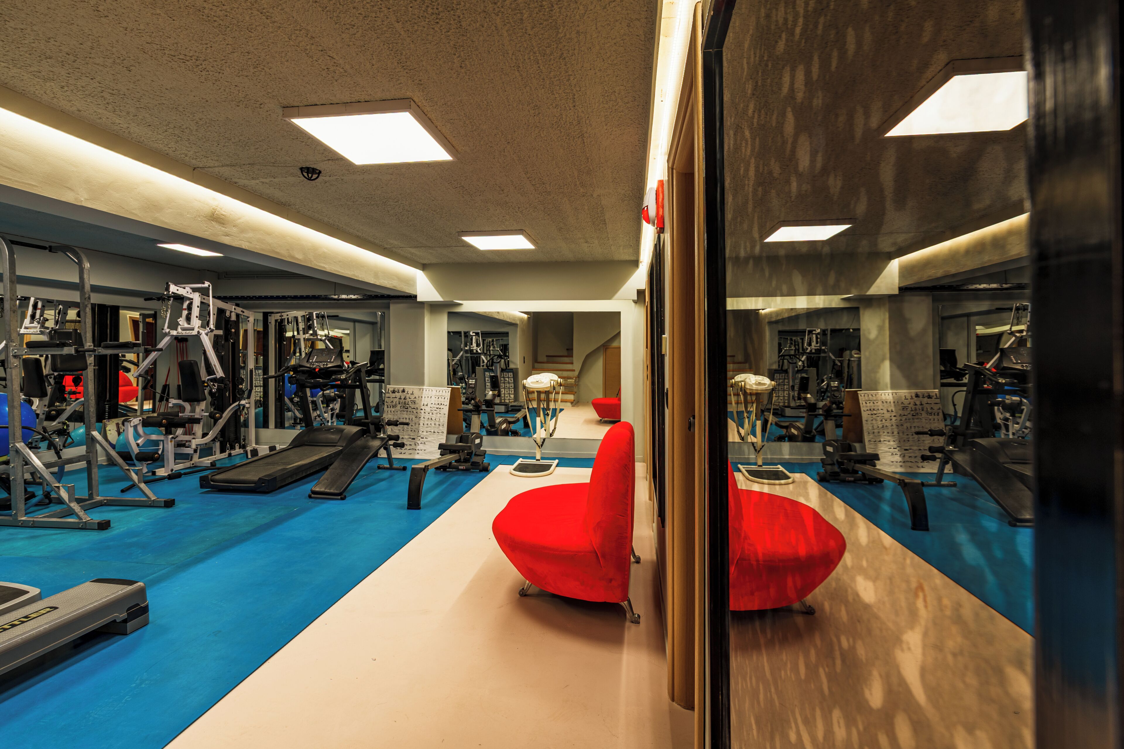 Ein Fitnessraum mit Trainingsgeräten, einem roten Stuhl und einem blauen Teppich.