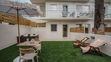 A two-story building with a balcony, a table with chairs, and a small garden area.