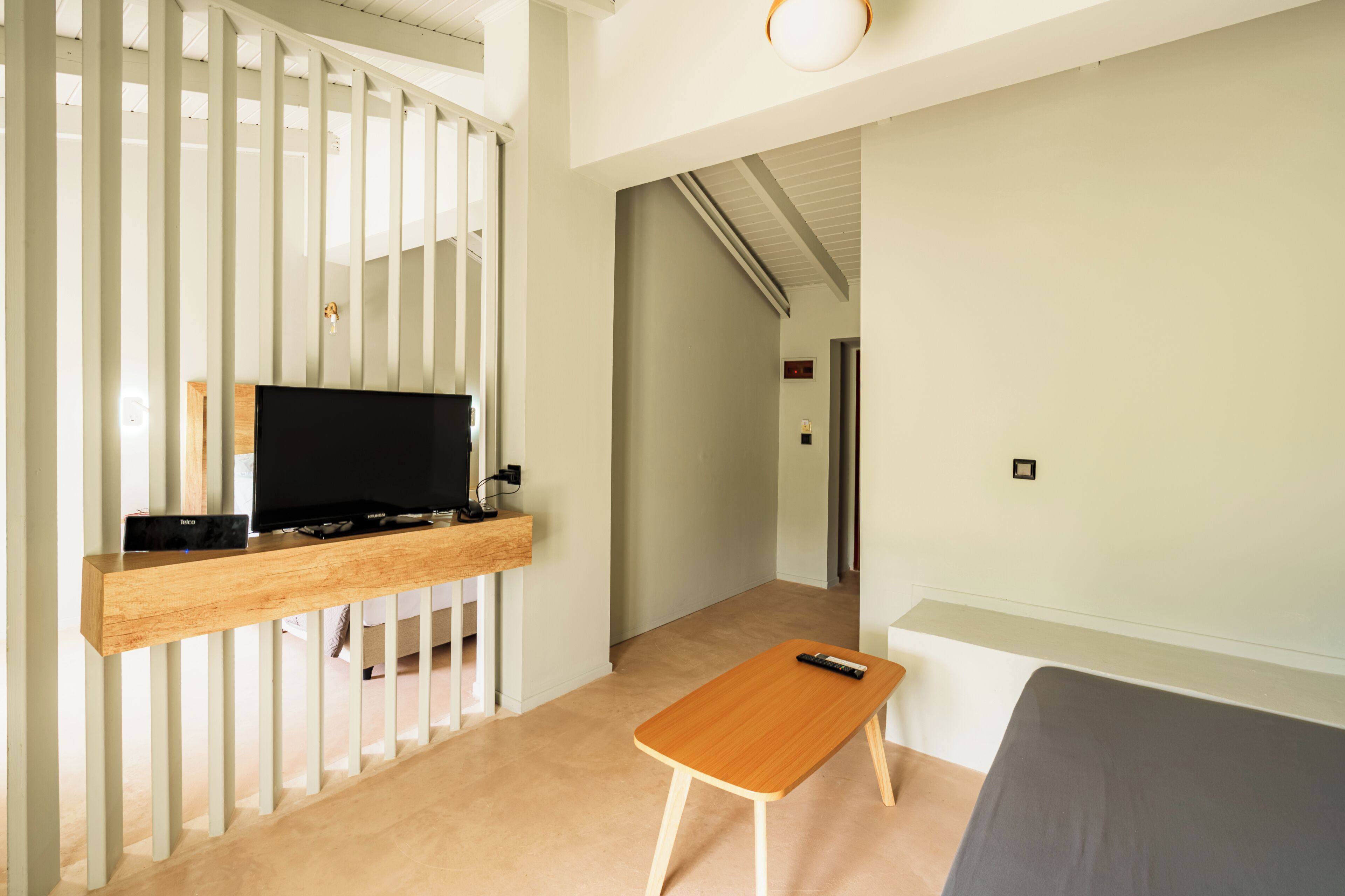 Une chambre moderne avec un téléviseur posé sur une étagère en bois, une petite table en bois et un canapé gris.