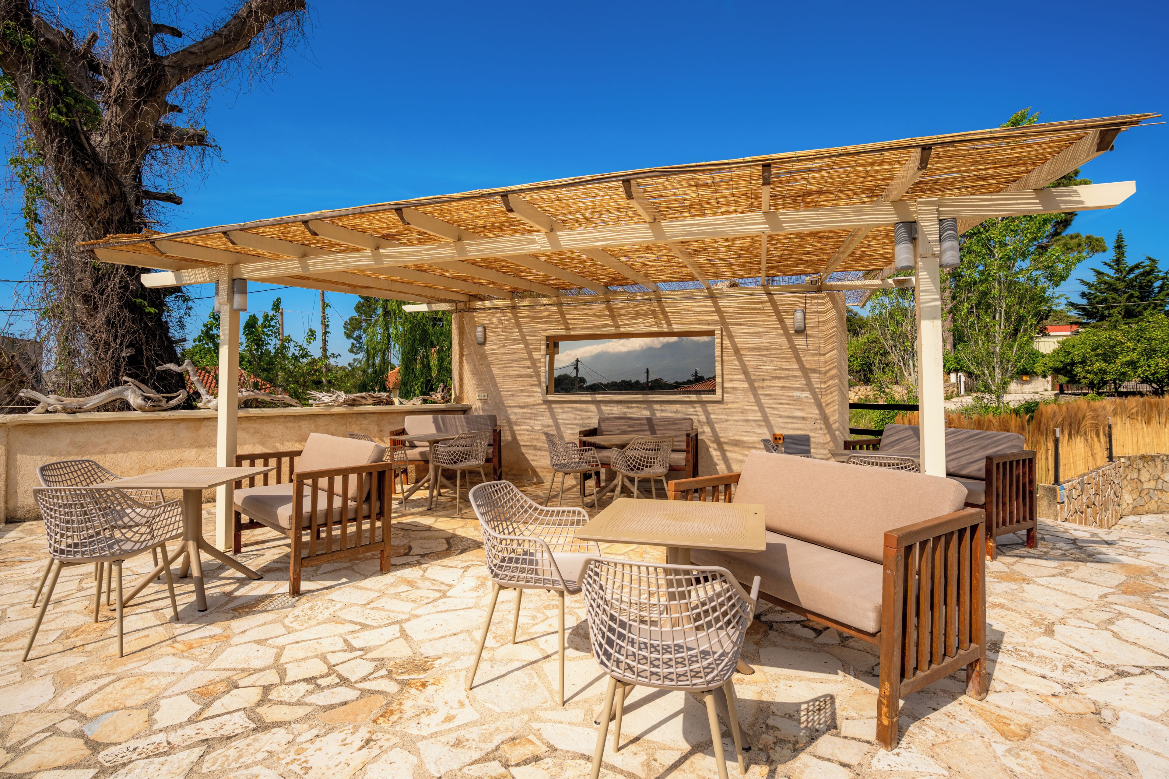 Eine Terrasse im Freien mit Steinboden, Holzmöbeln und einer Pergola.