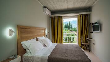 Une chambre d’hôtel avec un lit, un téléviseur fixé au mur et une fenêtre avec des rideaux.