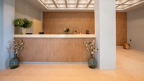 Un mostrador de recepción con un panel de madera decorativo, dos jarrones con flores y un techo con un diseño de luces geométricas.