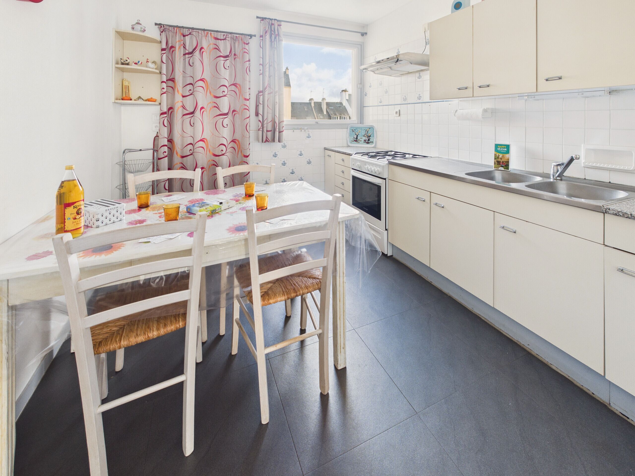 A modern kitchen with white cabinets, a gas stove, and a sink. There is a dining table with chairs and a window with curtains.