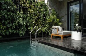 A modern indoor pool area with a wooden deck, a cushioned seating area, and a wall covered with lush green foliage. - Sunny Nine by Betterplace (Tibubeneng)