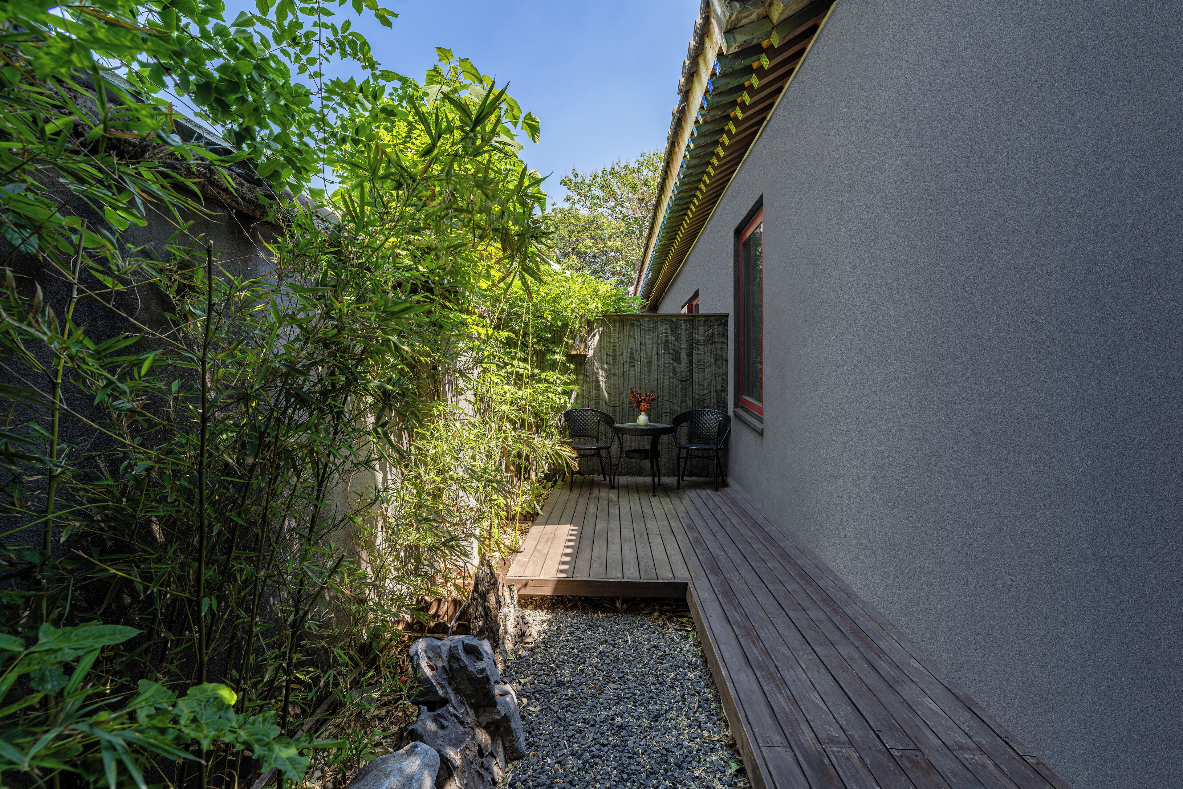 A patio with a table and chairs, surrounded by greenery and a stone pathway.