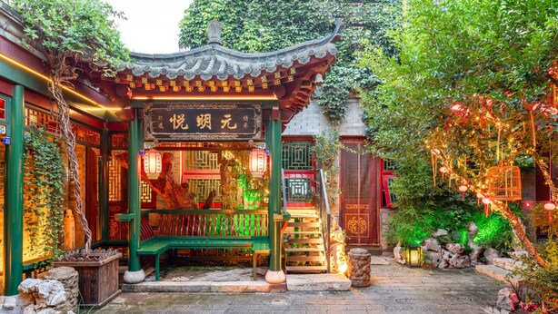 Um pavilhão tradicional chinês com telhado de azulejos, rodeado por vegetação exuberante e lanternas de pedra.