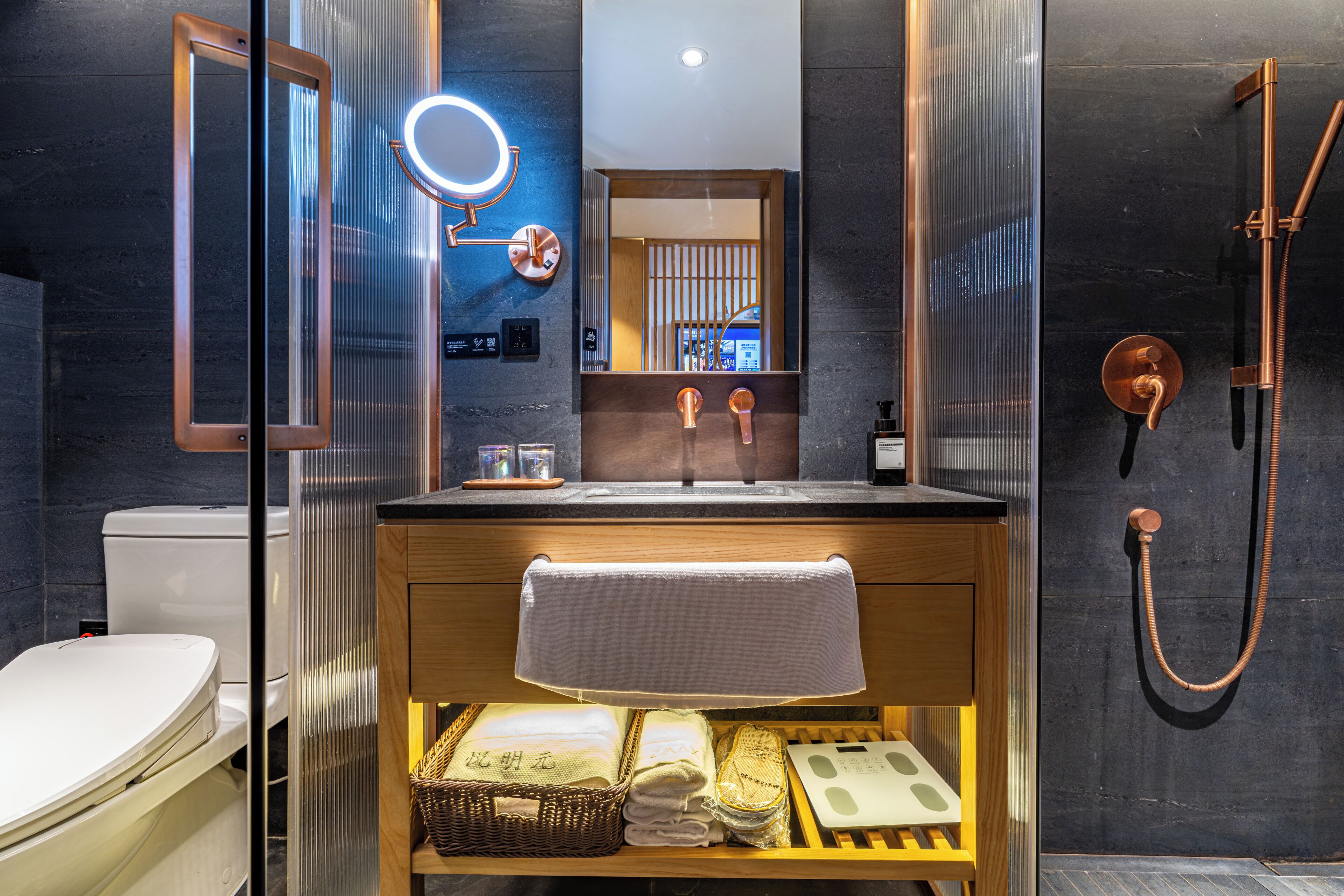 A modern bathroom with a glass-enclosed shower, a wooden vanity, and a mirror with a light.