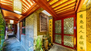 Um pátio tradicional chinês com chão de azulejos, plantas em vasos e uma porta vermelha com intrincado desenho em treliça.