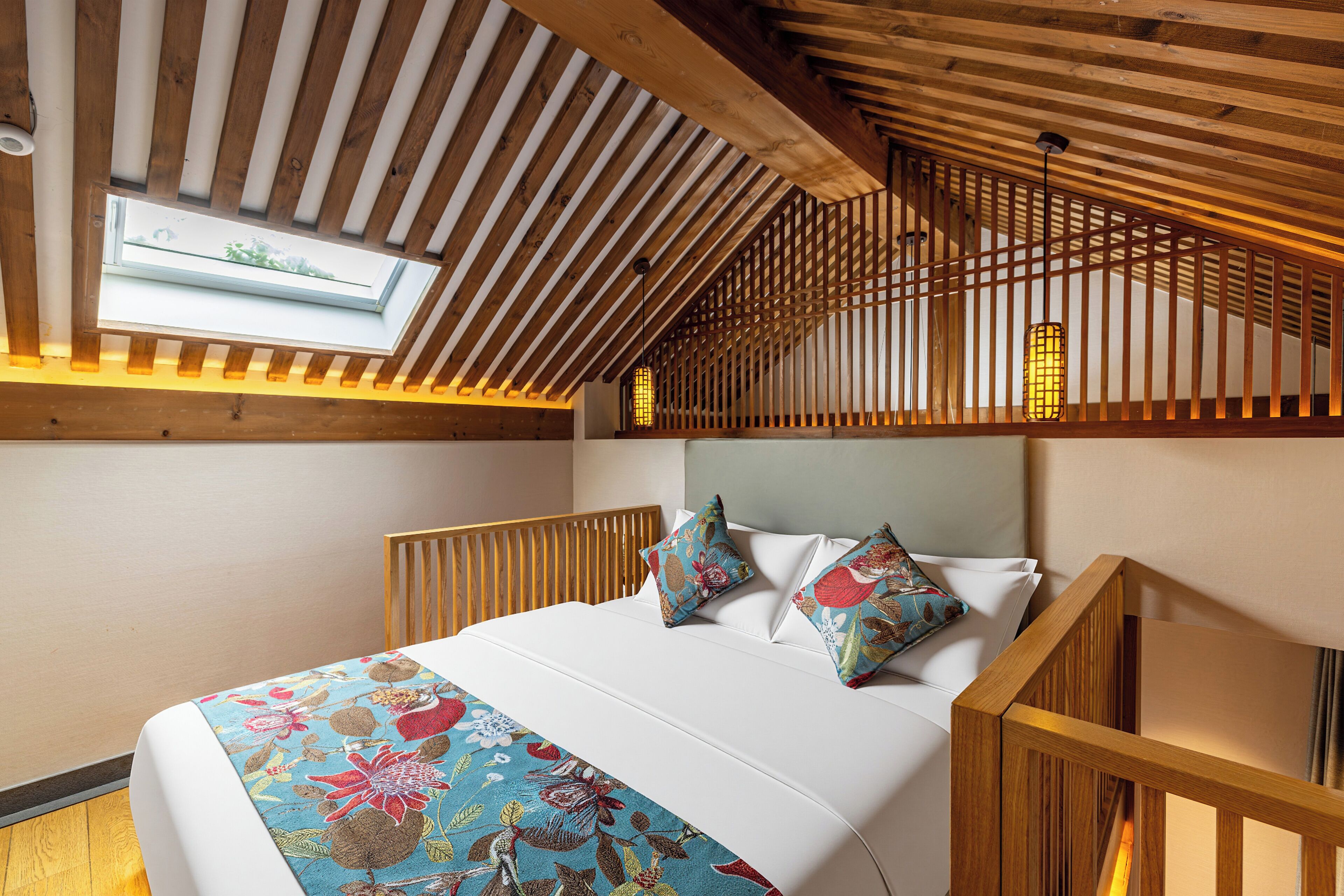 Ein Schlafzimmer mit geneigter Decke, einem Oberlicht, einem Bett mit floralem Bettzeug und einem Holz-Kopfstück.