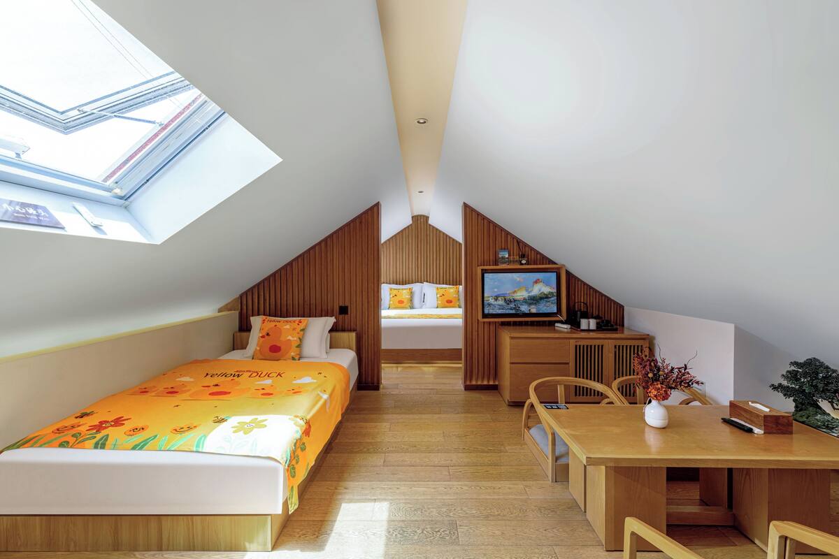 A bedroom with a skylight, a bed with a floral bedspread, a desk with a vase, and a television.