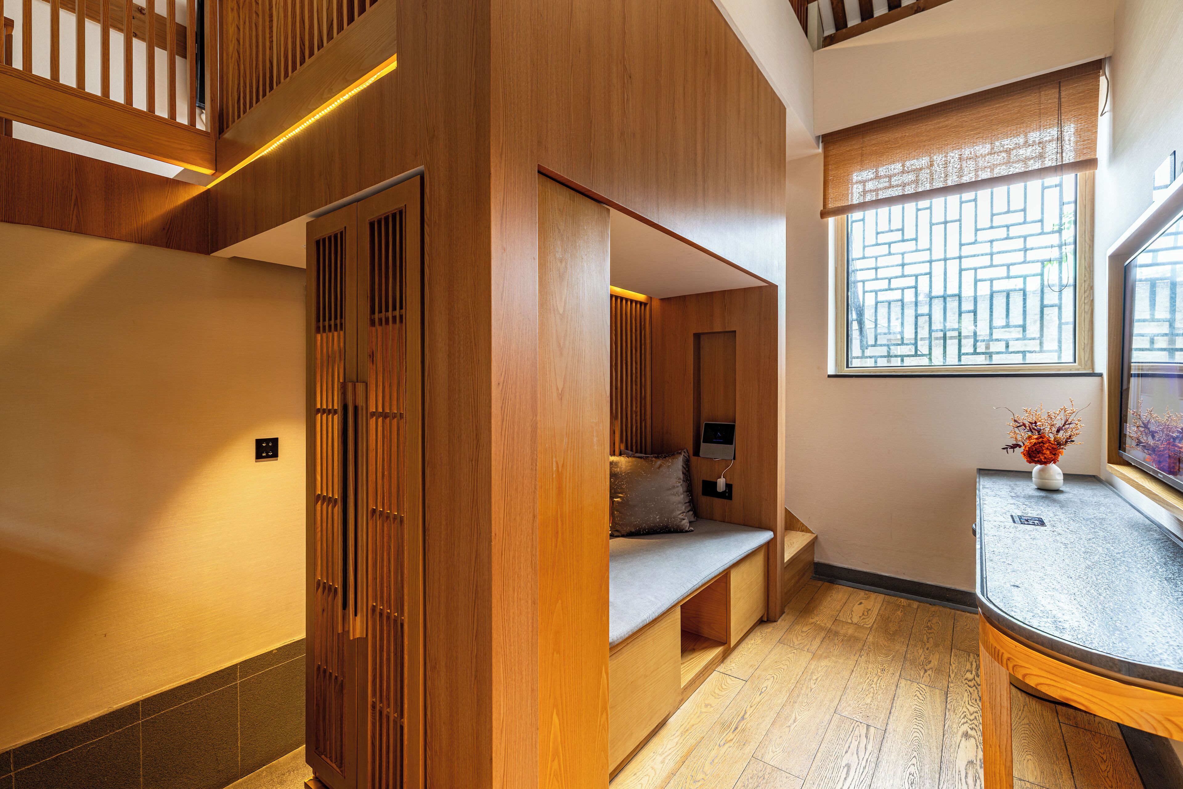 Un interior moderno con un banco de madera, una ventana con un diseño geométrico y una pequeña mesa con un florero.