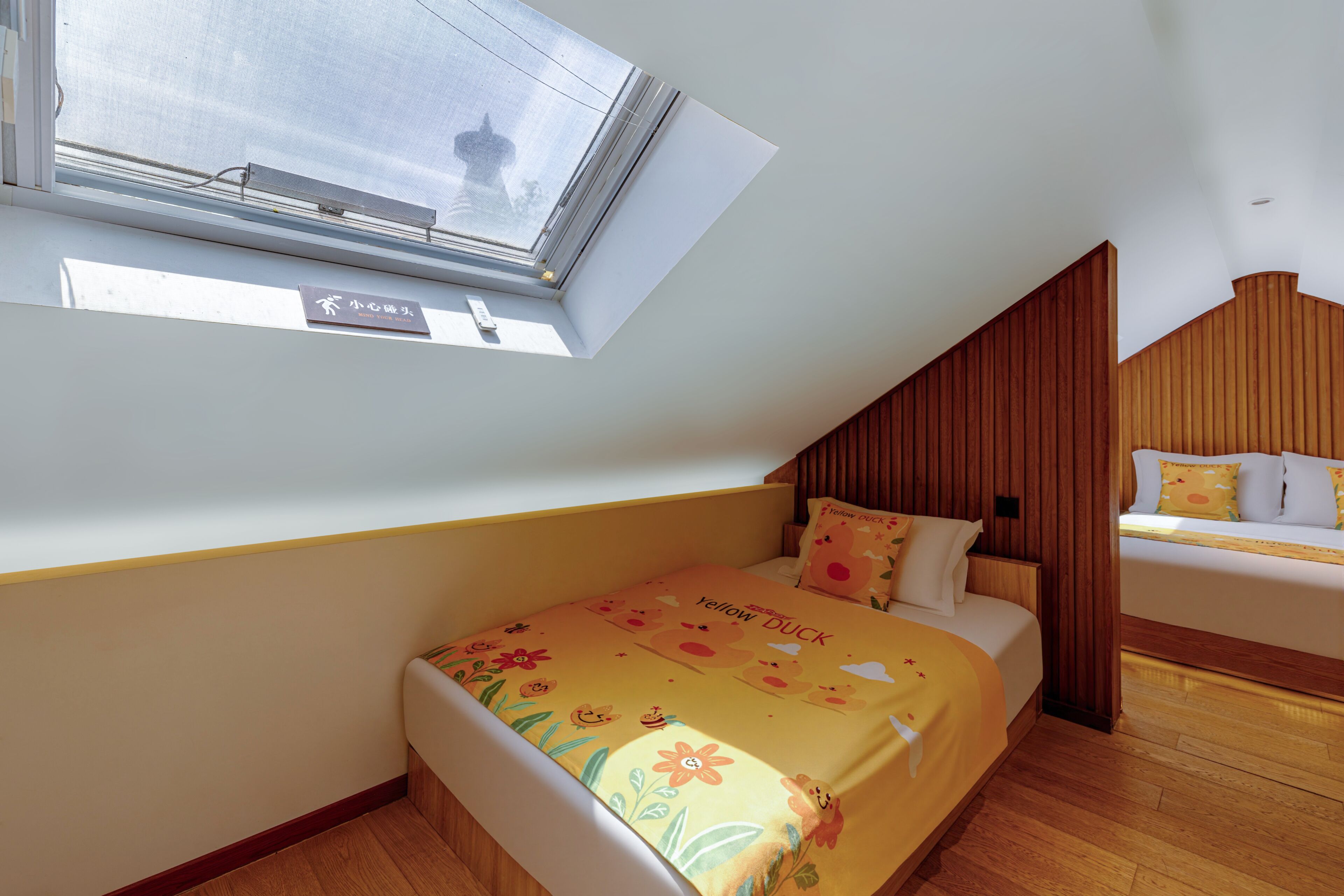 A bedroom with a sloped ceiling, a skylight, a bed with a yellow duck-themed bedspread, and wooden paneling.