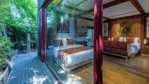 Quarto moderno com cama grande, piso de madeira e vista para um jardim através de uma parede de vidro.
