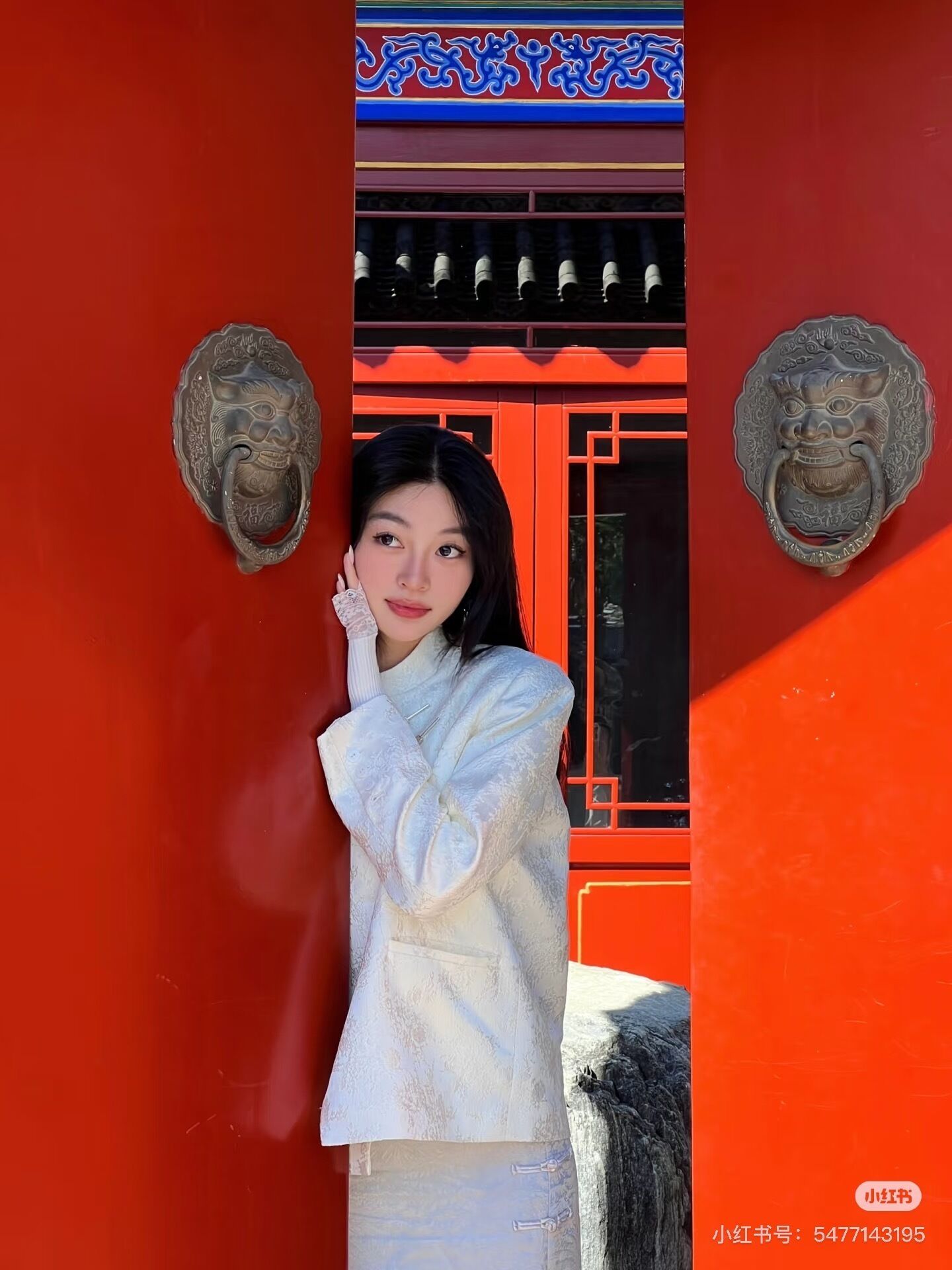 Una persona de pie frente a un edificio rojo con elementos arquitectónicos chinos tradicionales, incluyendo detalles ornamentales en los pomos de las puertas y diseños decorativos.