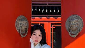 Una persona de pie frente a un edificio rojo con elementos arquitectónicos chinos tradicionales, incluyendo detalles ornamentales en los pomos de las puertas y diseños decorativos.