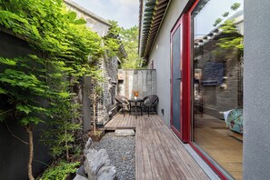 A patio with a table and chairs, a small garden area with plants and a rock feature, and a glass door leading to an interior space.