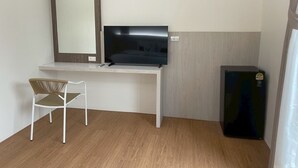 Een kleine, moderne kamer met een wit bureau, een televisie, een zwarte koelkast en een rieten stoel.