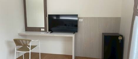 A small, modern room with a white desk, a television, a black refrigerator, and a wicker chair.
