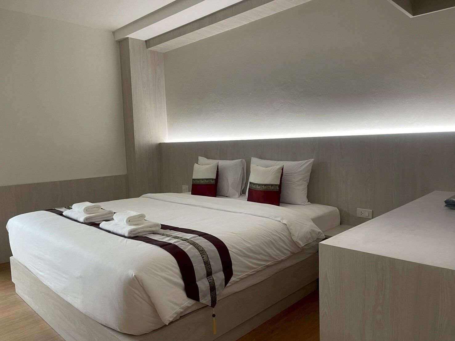 A modern hotel room with a bed, bedside table, and a built-in bench.