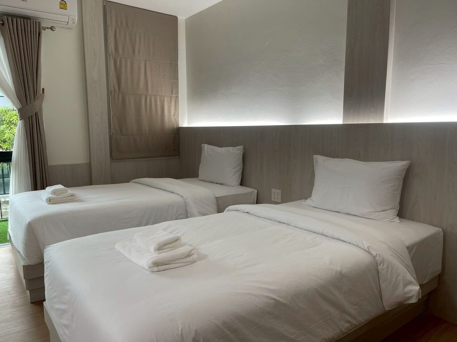 A hotel room with two beds, each with white linens and pillows, a wooden headboard, and a window with curtains.