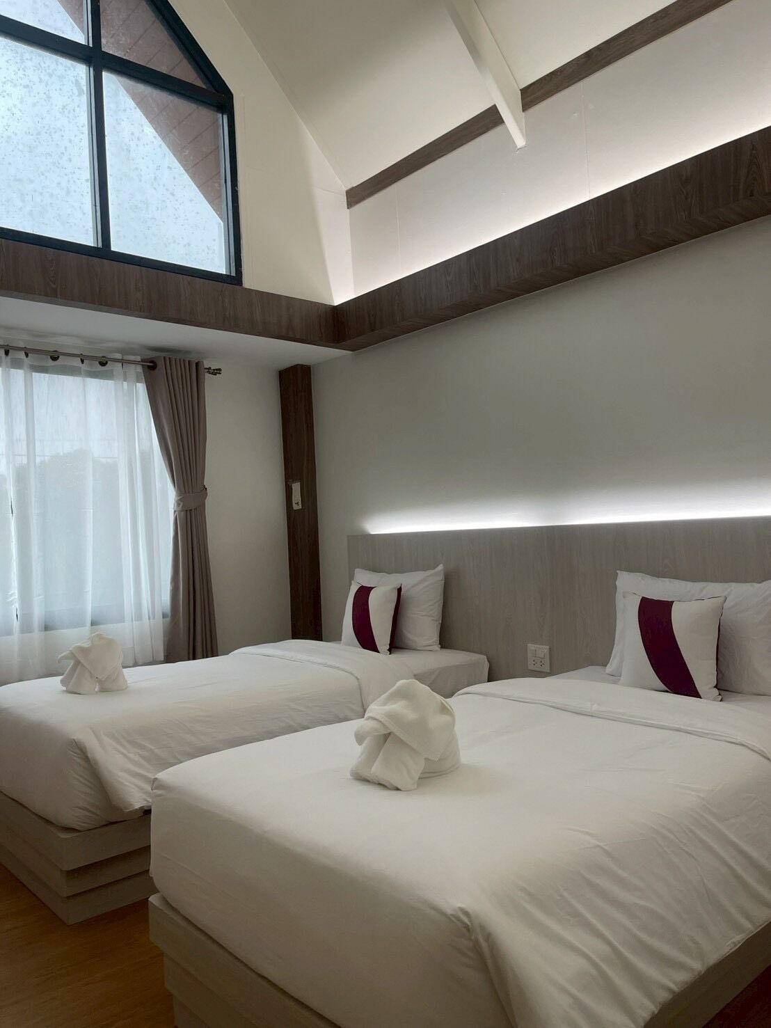 A hotel room with two beds, a large window with curtains, and a modern design.