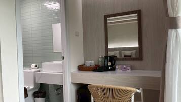 Un baño con lavamanos, inodoro y zona de ducha. Hay una silla y una mesita con artículos de aseo.