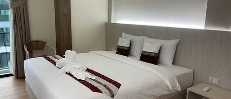 A modern hotel room with a large bed, a bedside table with a phone, and a view of the outdoors through the window.