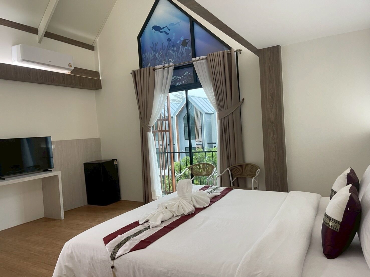A hotel room with a bed, a TV, a balcony with curtains, and a large window.