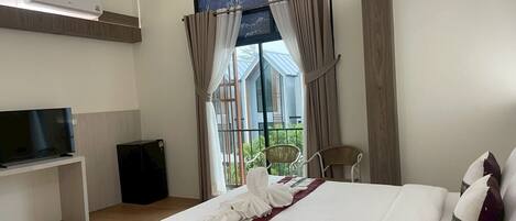 A hotel room with a bed, a TV, a balcony with curtains, and a large window.