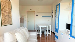 A white sofa, a dining table with chairs, and a TV on a cabinet. - Bibione Apartment With sea View (San Michele al Tagliamento)