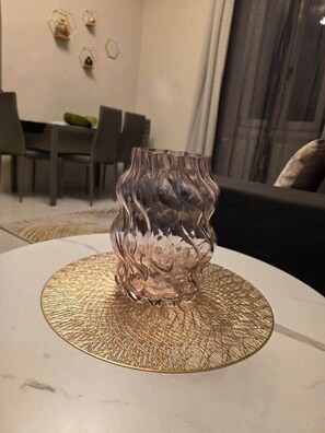 Een moderne woonkamer met een ronde tafel, een decoratieve glazen vaas en een eethoek op de achtergrond.