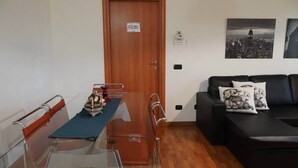 A compact living space with a dining table, a black leather sofa, and a cityscape painting on the wall. - Roma 1 Apartment - THE V Collection (Turate)