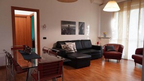 A living room with a black sofa, a red armchair, a glass dining table, and a wooden floor. - Roma 1 Apartment - THE V Collection (Turate)