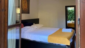 Une chambre à coucher avec un lit, un luminaire suspendu, un tableau au mur et une vue à travers une porte vitrée.