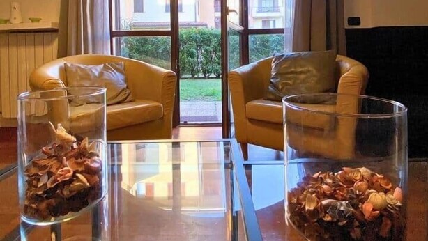 Un salon avec deux canapés en cuir, une table basse en verre et deux vases en verre contenant des fleurs séchées.