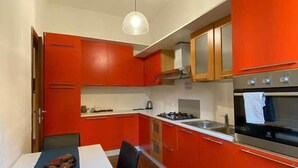 Une cuisine compacte avec des meubles rouges, un plan de travail blanc et un four en acier inoxydable.