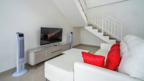A modern living room with a white sofa, red cushions, a flat-screen TV, and a staircase. - Luxury minimalist villa The Toy (Kerobokan)