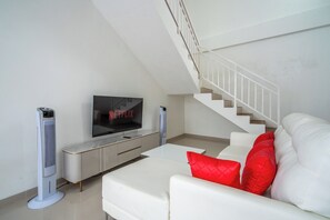 Un salon moderne avec un canapé blanc, des coussins rouges, un téléviseur à écran plat et un escalier.