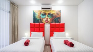 A hotel room with two beds, each with a red headboard, white bedding, and a rolled red towel. There is a large painting above the beds, and the room has a modern design with a white ceiling and walls. - Luxury minimalist villa The Toy (Kerobokan)