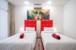 Une chambre d’hôtel avec deux lits, chacun doté d’une tête de lit rouge, de draps blancs et d’une serviette rouge enroulée. Un grand tableau est accroché au-dessus des lits, et la chambre présente un design moderne avec un plafond et des murs blancs.
