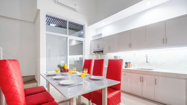 A modern kitchen with white cabinets, a glass dining table, and red upholstered chairs. - Luxury minimalist villa The Toy (Kerobokan)