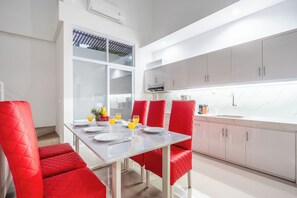 Une cuisine moderne avec des meubles blancs, une table à manger en verre et des chaises recouvertes d’un tissu rouge.