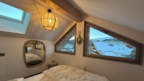 A bedroom with a bed, a skylight, a hanging light fixture, a mirror, and a window with a snowy landscape view. - Quartz 404 by Avecoeur (Huez)