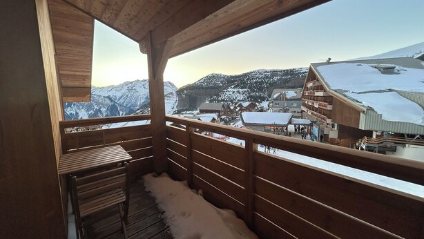 A wooden balcony with a view of a snow-covered mountain and buildings. - Quartz 404 by Avecoeur (Huez)