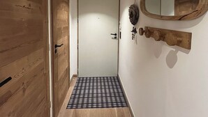 A hallway with wooden flooring, a checkered mat, a white door, and a wooden wall-mounted mirror. - Quartz 404 by Avecoeur (Huez)